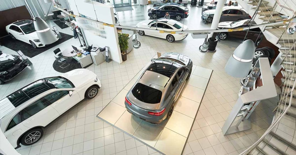 Overhead view of a car showroom captured by a security camera, showcasing vehicles on display, desks, and a staircase, emphasizing surveillance coverage.