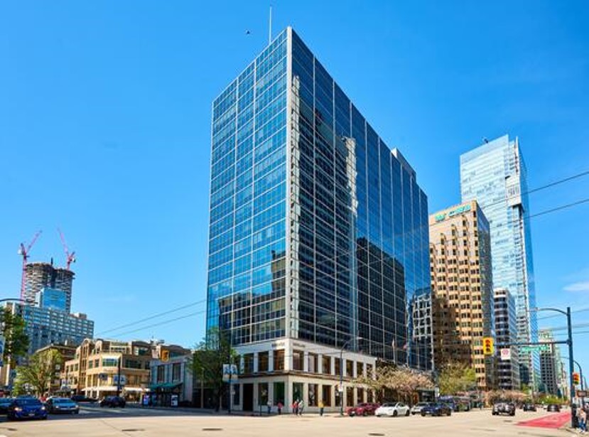 A modern office building with a glass facade in an urban setting, surrounded by other high-rise structures and clear blue skies.