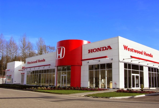 Westwood Honda dealership featuring a modern design with red and white branding, large glass windows, and a spacious exterior under a clear blue sky.