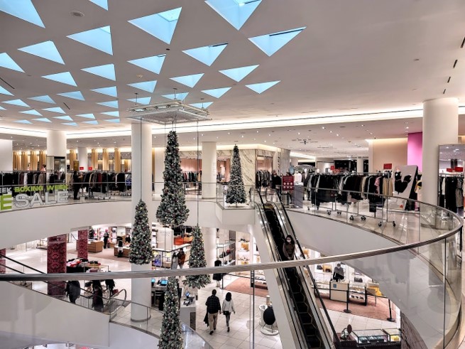 Interior view of a modern department store featuring holiday decorations, escalators, and skylights with triangular designs.