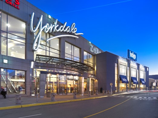 Exterior view of Yorkdale Shopping Centre at dusk, featuring illuminated signage and storefronts, including Zara and Indigo.