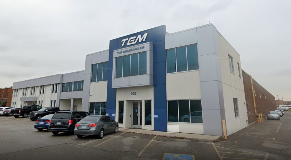 Exterior view of a commercial building labeled "TGM - Top Grade Molds," with a parking lot in the foreground.