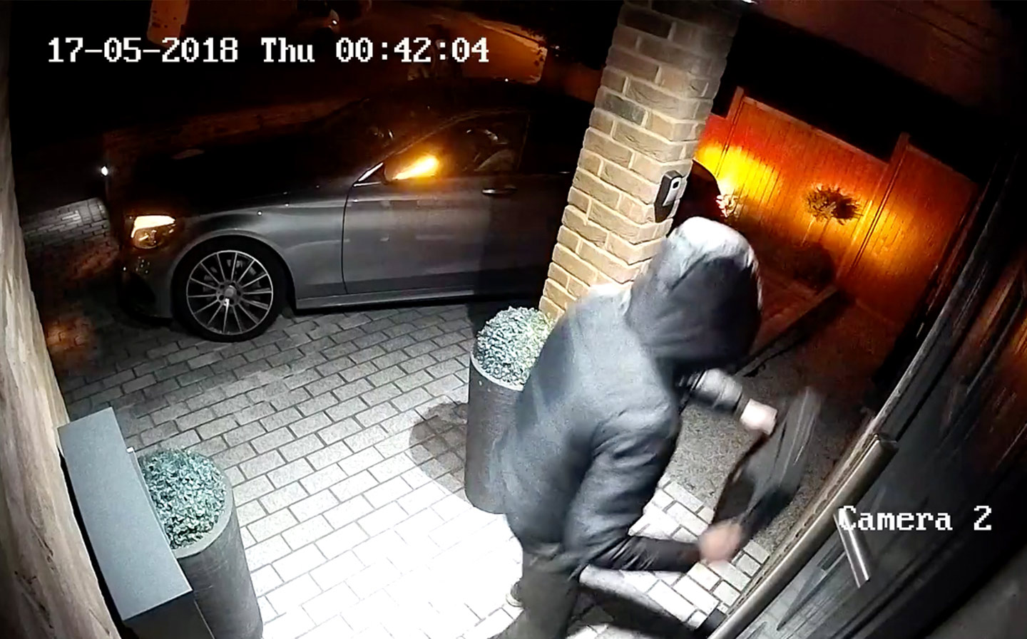 CCTV footage of a hooded individual attempting to break into a property at night.