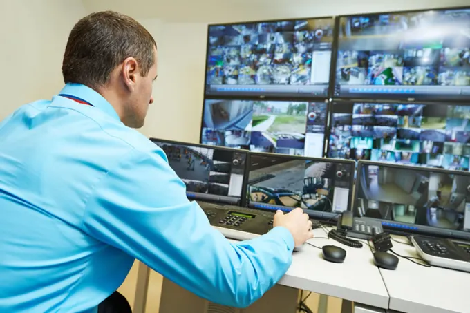 A security professional monitoring multiple live CCTV feeds on a control panel with multiple screens.