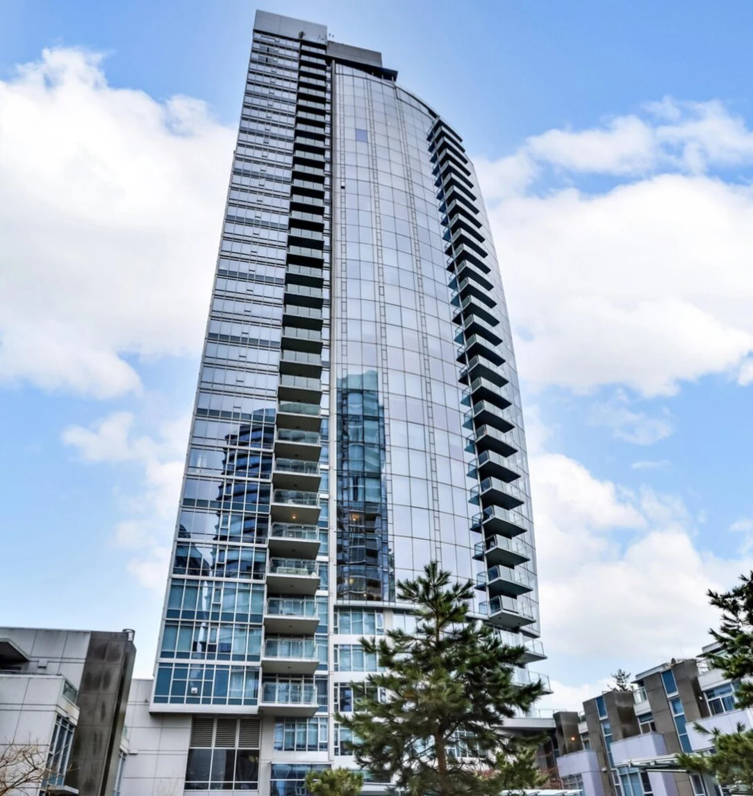 Modern high-rise condominium building with glass facade and multiple balconies under a clear sky.